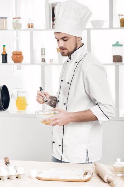 Yumurta ve süt kase mutfakta kırbaçlanan üniforma şef