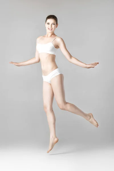 Szczupła, piękna kobieta z idealne ciało w białej bieliźnie skoki na szarym tle — Zdjęcie stockowe