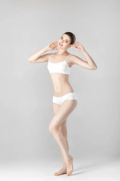 Mujer hermosa delgada con cuerpo perfecto en lencería blanca sobre fondo gris — Foto de Stock