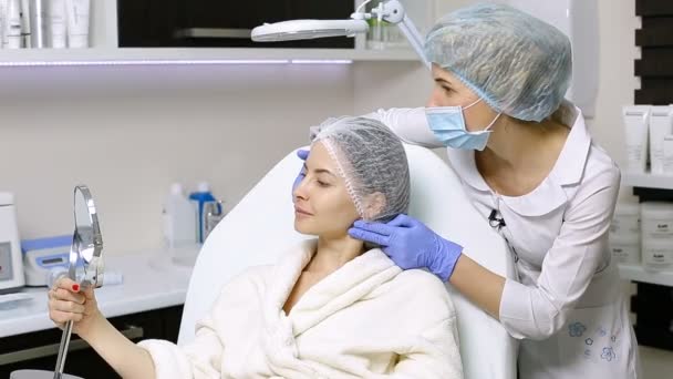 Mooie vrouw bekijkt zichzelf in de spiegel na cosmetische ingrepen in de schoonheidssalon — Stockvideo