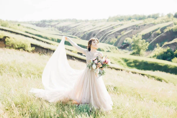 Bellas artes fotografía de boda. Hermosa novia con ramo y vestido con tren en la naturaleza — Foto de Stock