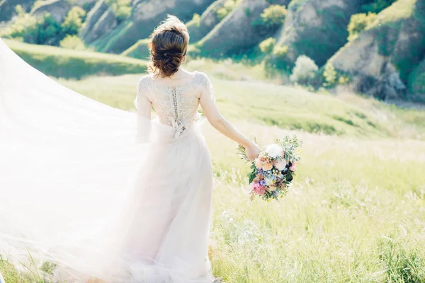 Bellas artes fotografía de boda. Hermosa novia con ramo y vestido con tren en la naturaleza — Foto de Stock