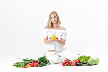 Beyaz elbise ve beyaz arka plan üzerinde taze sebze güzel sarışın kadın. Dolmalık biber kız tutar