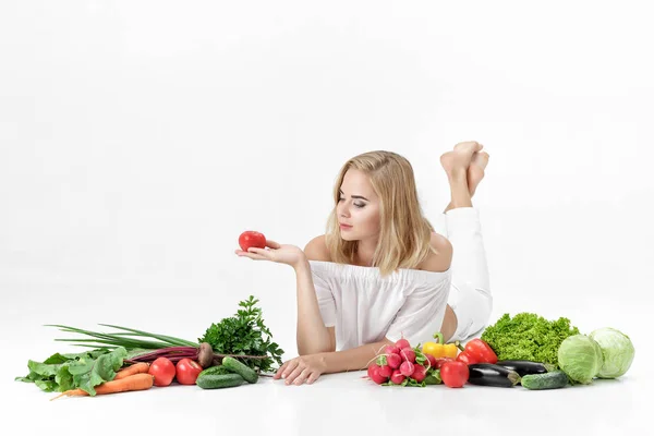 Vacker blond kvinna i vita kläder och massor av färska grönsaker på vit bakgrund. Flicka innehav tomat — Stockfoto