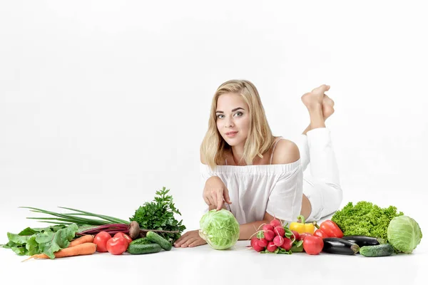 Belle femme blonde en vêtements blancs et beaucoup de légumes frais sur fond blanc — Photo