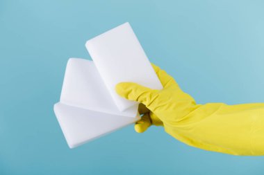 sünger mavi arka plan üzerinde tutan bir sarı lastik eldiven el.