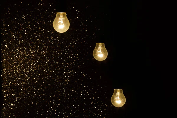 Light bulbs on a black background with sparkles — Stock Photo, Image