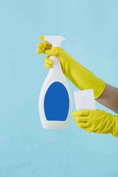 Sárga kesztyű kéz tartja a spray palack, folyékony mosószer és szivacs a kék háttér. takarítás — Stock Fotó