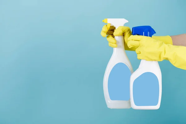 Hand i gul handske håller sprayflaska med flytande tvättmedel på blå bakgrund. rengöring — Stockfoto