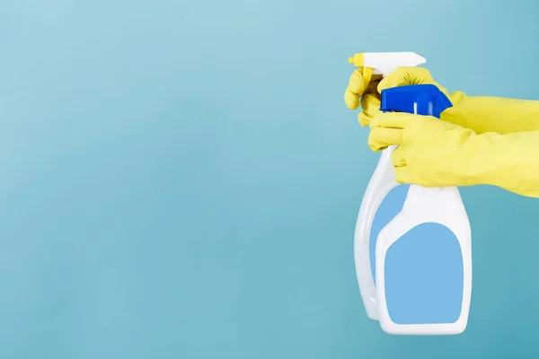 Mano in guanto giallo tiene bottiglia spray di detergente liquido su sfondo blu. pulizia — Foto Stock