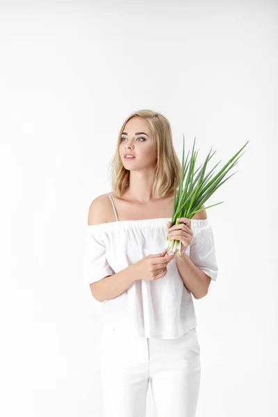 Krásná blonďatá žena v bílé halence drží cibule na bílém pozadí. Zdraví a vitamíny — Stock fotografie
