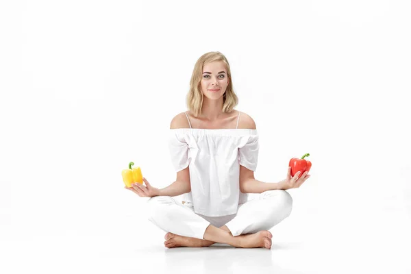 Beautiful blond woman in white blouse chooses yellow or red bell pepper. Health and Diet Stock Photo