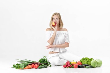 Beyaz elbise ve beyaz arka plan üzerinde taze sebze güzel sarışın kadın. Kız nektarin yiyor