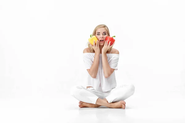 Piękne blond kobieta w białej bluzce trzyma żółtej i czerwonej papryki. Zdrowa dieta i dieta — Zdjęcie stockowe