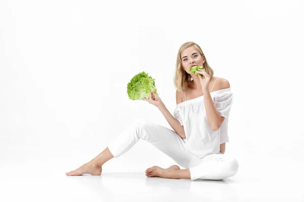 Hermosa mujer rubia en blusa blanca comiendo ensalada verde fresca sobre fondo blanco. Salud y dieta — Foto de Stock