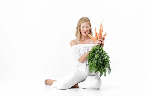 Belle femme blonde tenant carotte fraîche avec des feuilles vertes sur fond blanc. Santé et alimentation — Photo