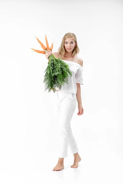 Hermosa mujer rubia sosteniendo zanahoria fresca con hojas verdes sobre fondo blanco. Salud y dieta — Foto de Stock