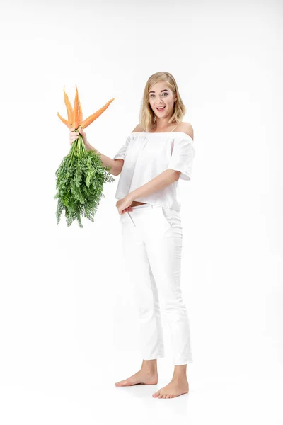 Mujer rubia sosteniendo zanahoria fresca con hojas verdes sobre fondo blanco. chica come zanahorias y se adelgaza — Foto de Stock