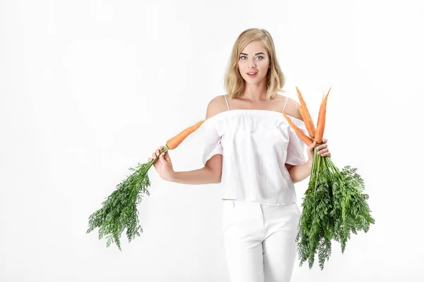 Belle femme blonde tenant carotte fraîche avec des feuilles vertes sur fond blanc. Santé et alimentation — Photo