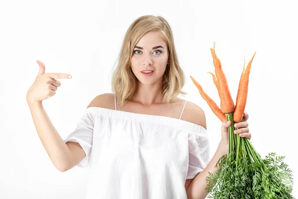 Schöne blonde Frau zeigt eine frische Karotte mit grünen Blättern auf weißem Hintergrund. Gesundheit und Ernährung — Stockfoto