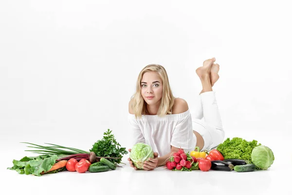 Vacker blond kvinna i vita kläder och massor av färska grönsaker på vit bakgrund — Stockfoto