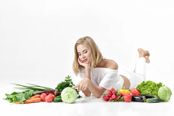 Piękne blond kobieta w białe szaty i mnóstwo świeżych warzyw na białym tle — Zdjęcie stockowe