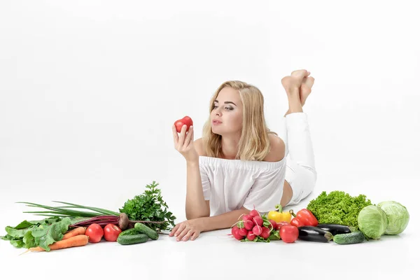 Schöne blonde Frau in weißen Kleidern und viel frisches Gemüse auf weißem Hintergrund. Mädchen mit Tomate — Stockfoto