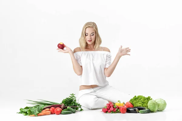 Femme blonde surprise en vêtements blancs et beaucoup de légumes frais sur fond blanc. fille mange nectarine — Photo