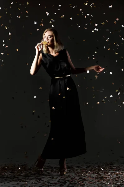 Belle femme blonde heureuse tenant un verre de vin blanc sur fond noir avec des confettis — Photo