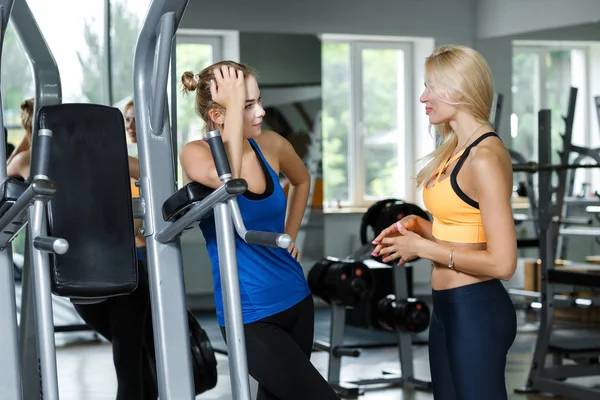 Två atletisk blonda kvinnor talar i gymmet. Flicka kommunicerar med tränare — Stockfoto
