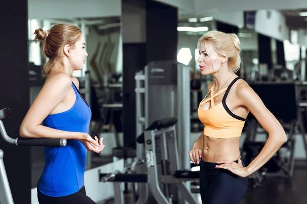 Δύο αθλητικά ξανθά γυναίκες μιλούν στο γυμναστήριο. Κορίτσι επικοινωνεί με εκπαιδευτή — Φωτογραφία Αρχείου