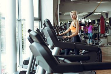 spor salonunda treadmill çalıştıran atletik sarışın kadın.