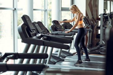 spor salonunda treadmill çalıştıran atletik sarışın kadın.