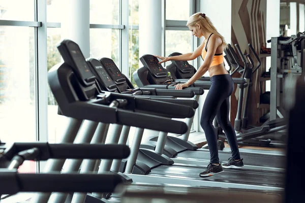 spor salonunda treadmill çalıştıran atletik sarışın kadın.