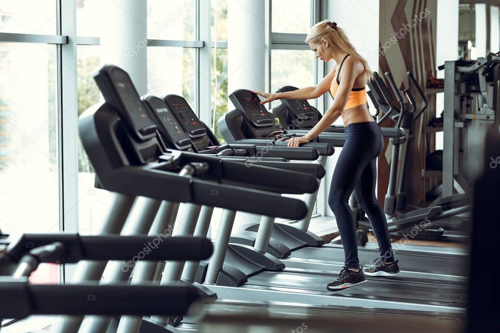 athletic blond woman running on treadmill at gym.