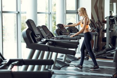 spor salonunda treadmill çalıştıran atletik sarışın kadın.