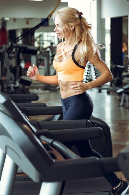 spor salonunda treadmill çalıştıran atletik sarışın kadın.