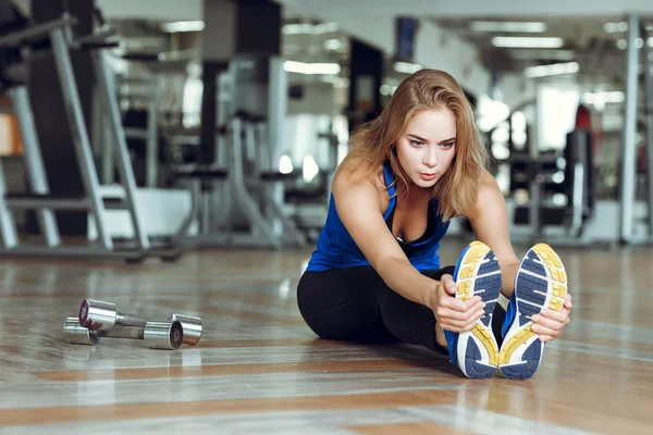 Νεαρή λεπτή ξανθιά γυναίκα κάνει ασκήσεις στο γυμναστήριο — Φωτογραφία Αρχείου