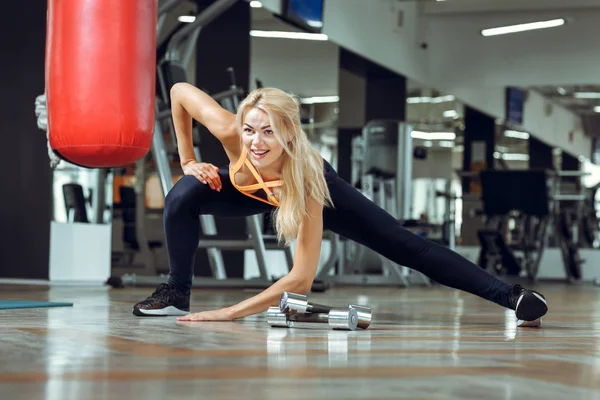 Νεαρή λεπτή ξανθιά γυναίκα κάνει ασκήσεις στο γυμναστήριο — Φωτογραφία Αρχείου