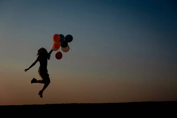 Silhouette einer jungen Frau mit fliegenden Ballons gegen den Himmel. — Stockfoto