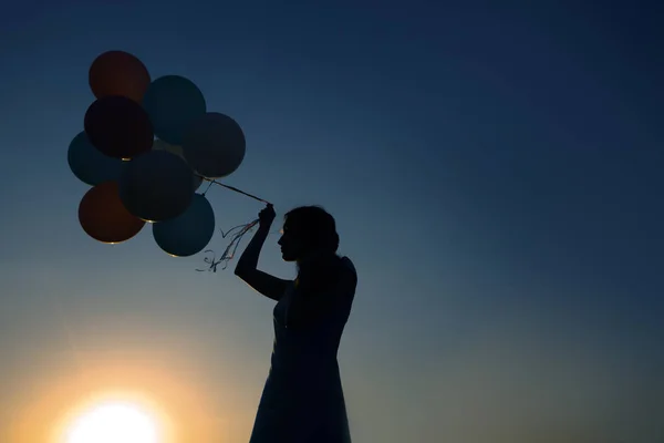 Silhouette einer jungen Frau mit fliegenden Ballons gegen den Himmel. — Stockfoto