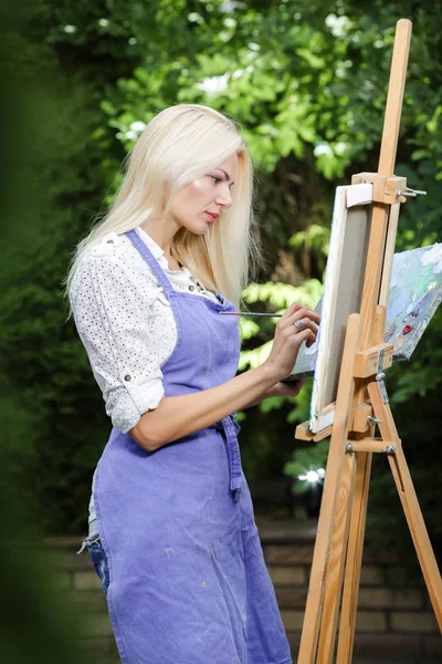 Женщина-художник с кистью в руке рисует на холсте — стоковое фото