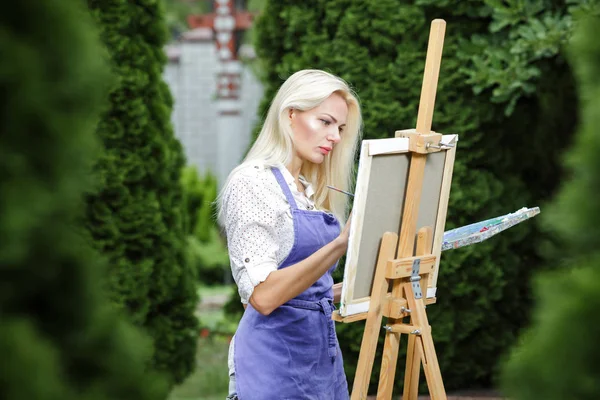 Женщина-художник с кистью в руке рисует на холсте — стоковое фото