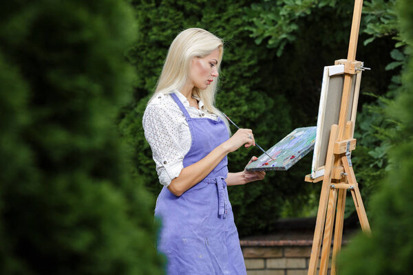 Женщина-художник с кистью в руке рисует на холсте
