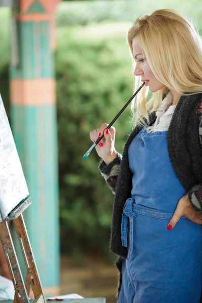 Žena umělec s kartáčem v ruce kreslí na plátně — Stock fotografie