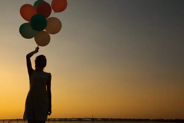 Silhouette einer jungen Frau mit fliegenden Ballons gegen den Himmel. — Stockfoto