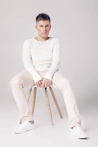 Joven guapo en suéter blanco se sienta en una silla en — Foto de Stock