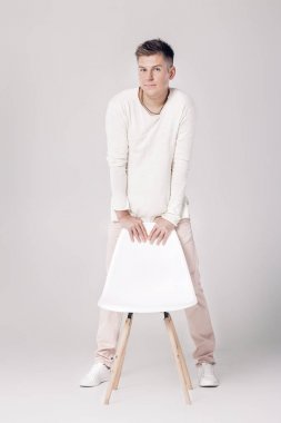 yakışıklı genç adam beyaz kazaklı bir sandalyeye oturur