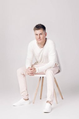 yakışıklı genç adam beyaz kazaklı bir sandalyeye oturur