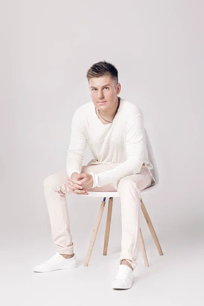 Красивий молодий чоловік у білому светрі сидить на стільці на — стокове фото